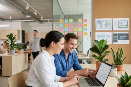 Deux collaborateurs d'une agence web travaillant ensemble sur la conception d'un site vitrine devant un ordinateur portable dans un bureau moderne