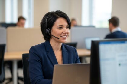 Conseillère clientèle en blazer marine avec casque sans fil, concentrée lors d'un appel téléphonique dans un bureau moderne en open space