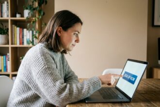 Femme pointant du doigt un bouton cliquable sur un écran d'ordinateur portable dans un bureau à domicile